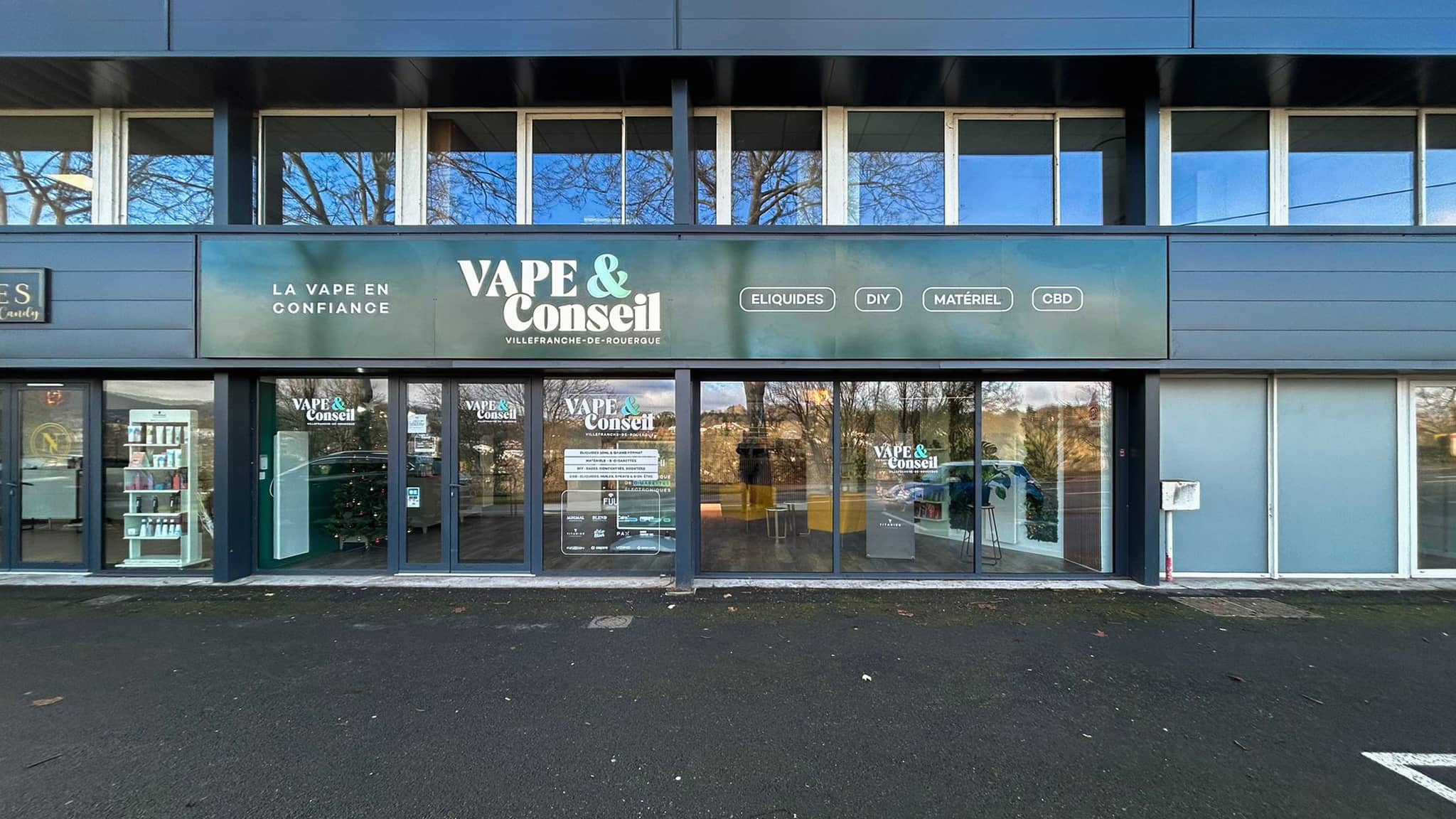 La devanture de Vape & Conseil, avenue du Quercy : enseigne lumineuse et places de stationnement devant le magasin.
